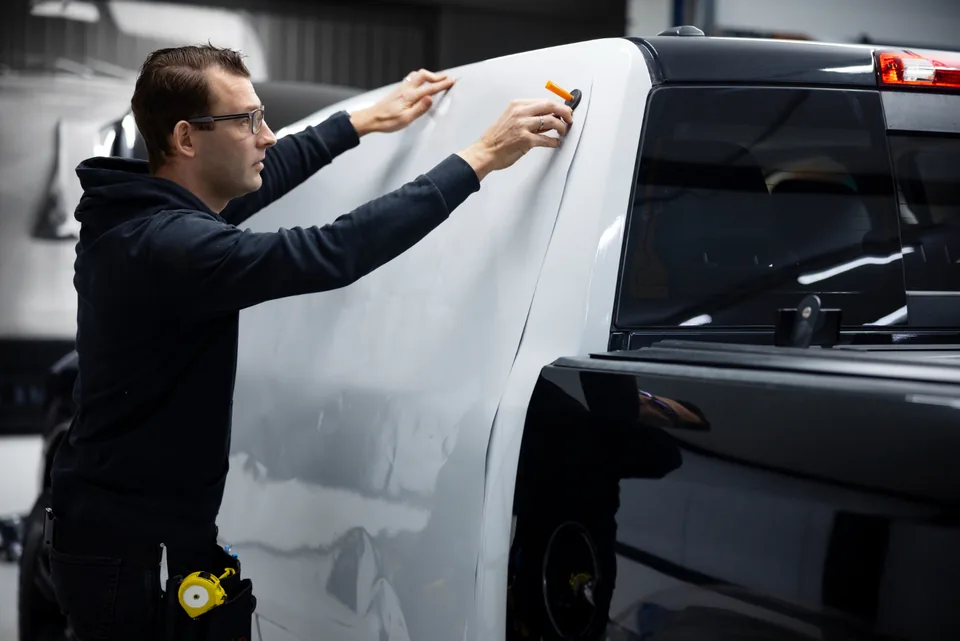 Installer smoothing white vinyl along the bed side of a pickup truck inside a shop bay