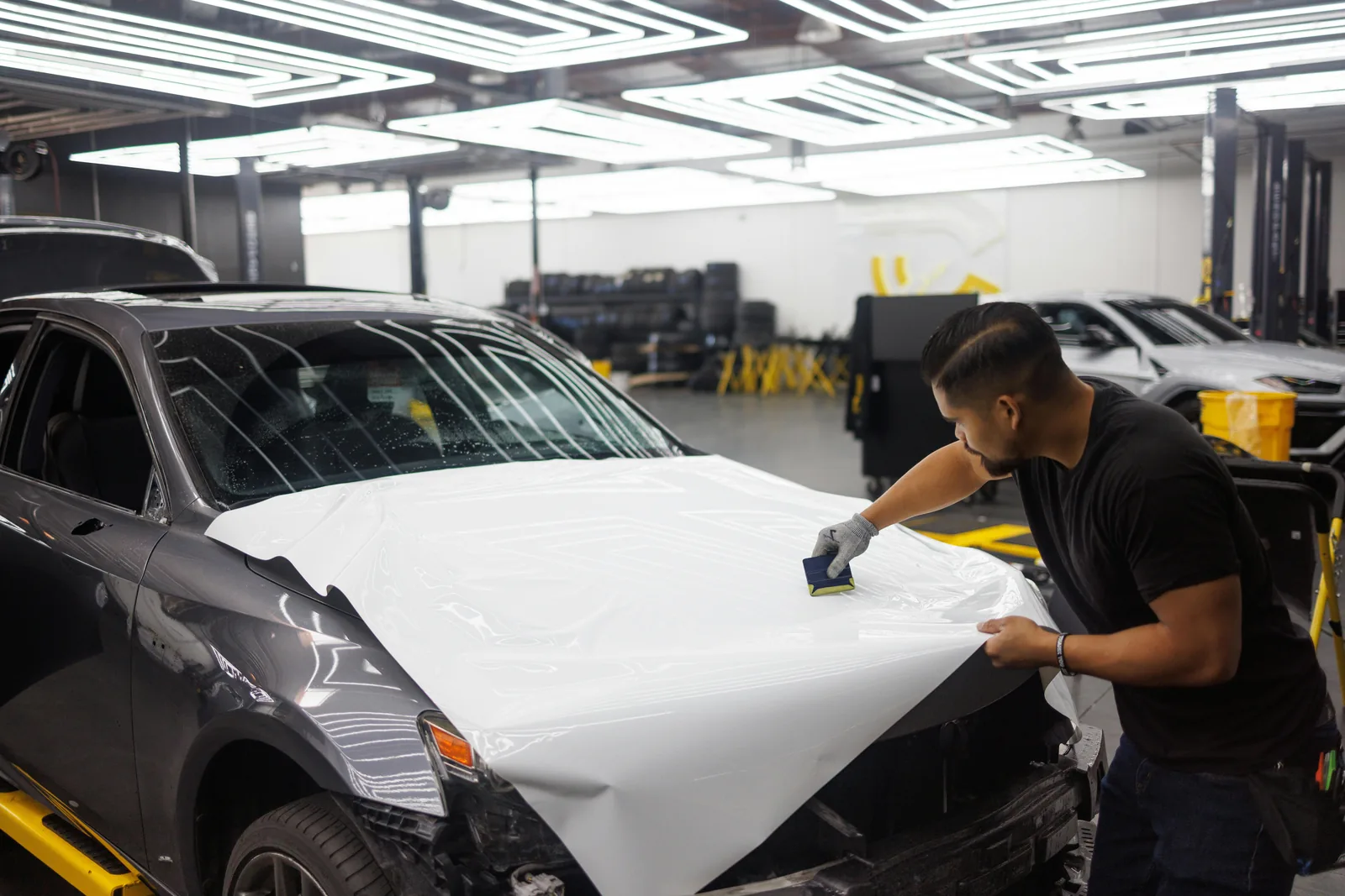 Installer working a sheet of white gloss vinyl across the hood of a dark grey SUV