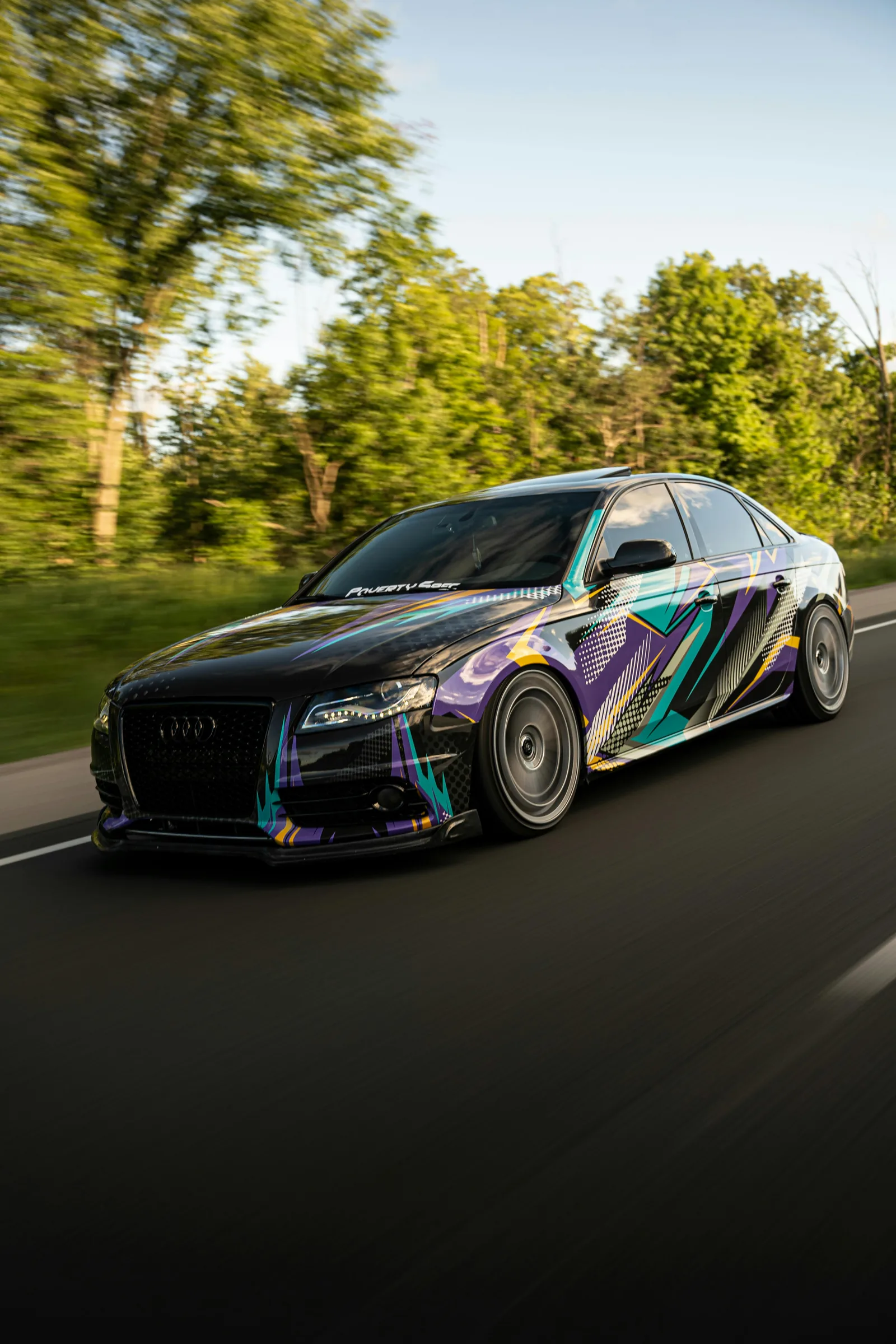 Black Audi S4 finished in a purple, teal and yellow geometric printed wrap, photographed rolling on a road