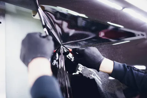 Gloved hands heat shrinking tint film with fingers spread across a curved rear window