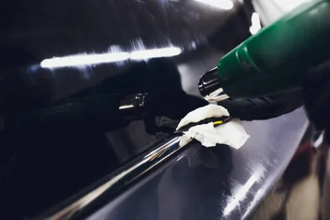 Heat gun and cloth being used to work vinyl film along the belt line of a car window