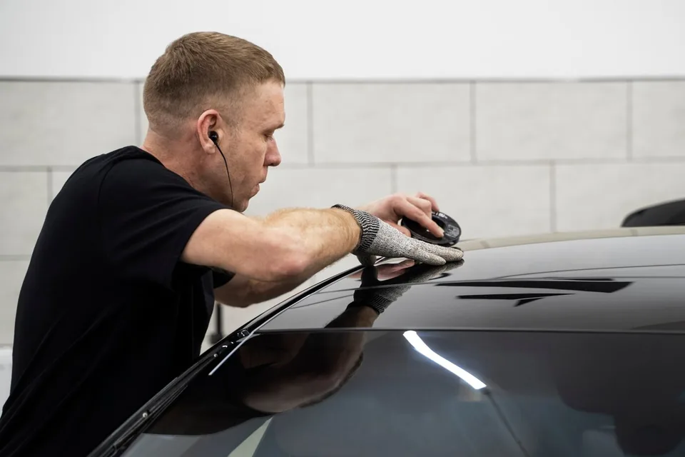 Installer buffing along the roof edge of a dark car with a hand pad