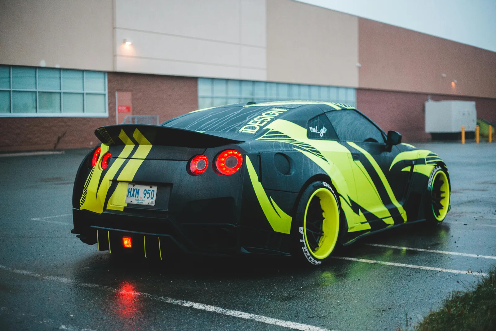 Nissan GT-R finished in a black and high visibility yellow graphic livery, rear three quarter view on a wet lot