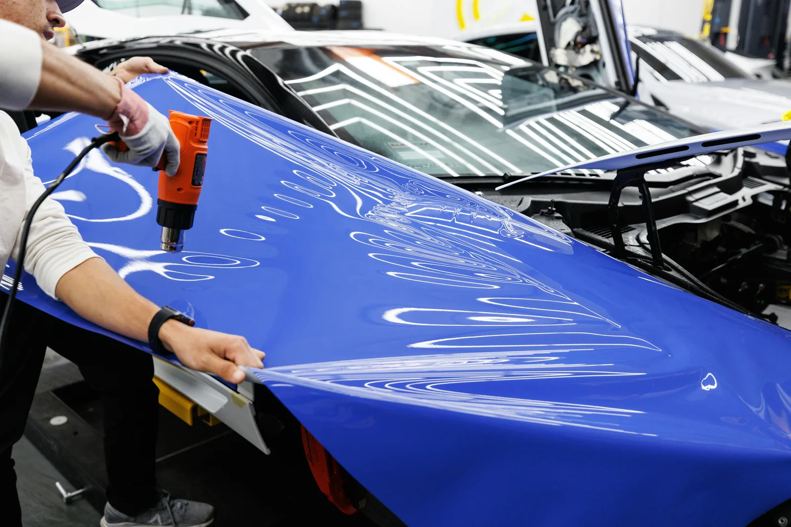 Installer using a heat gun and squeegee to work blue gloss vinyl over a car hood