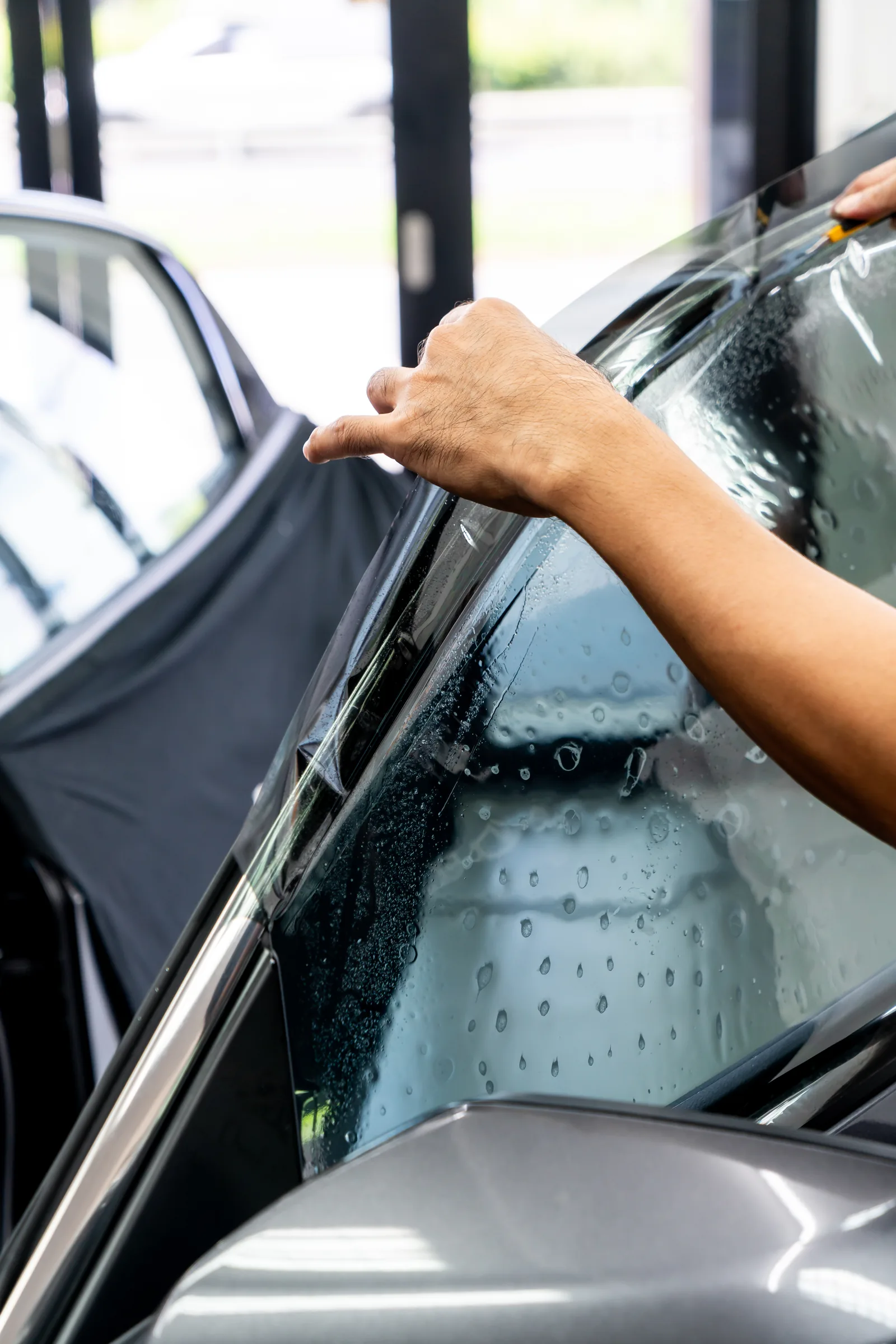 Installer sliding a wet sheet of tint film onto the front door glass of a dark car