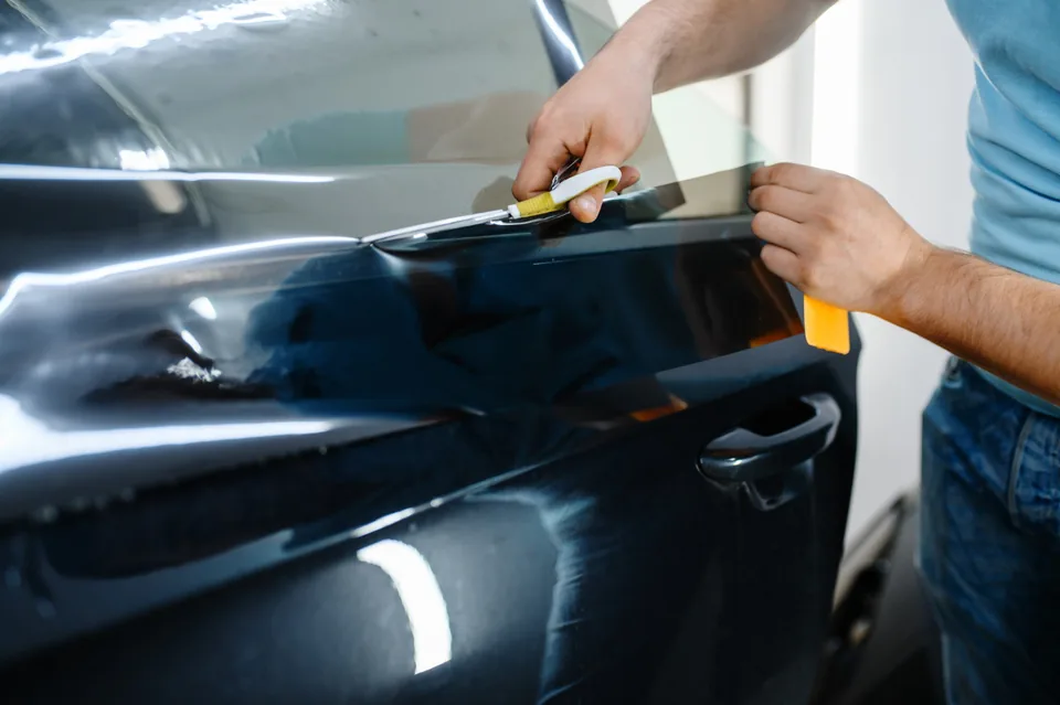 Squeegee and blade trimming tint film along the top edge of a car door window